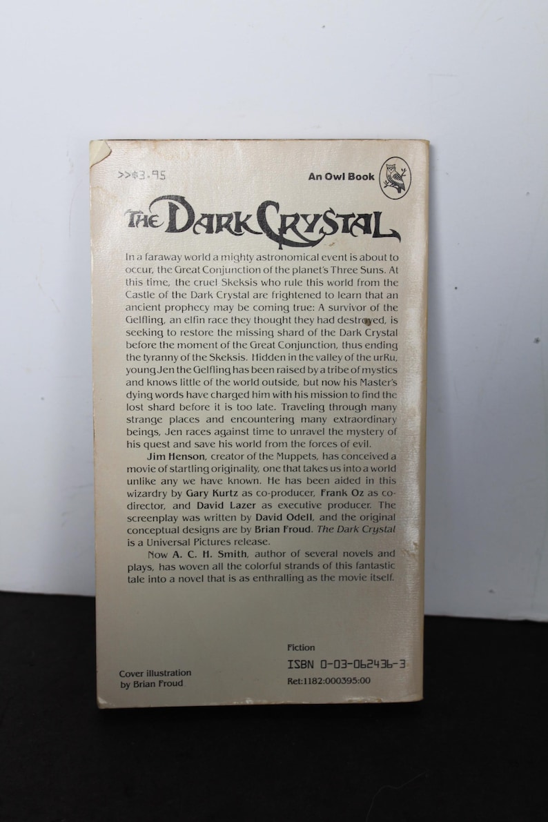 May include: A paperback book titled "The Dark Crystal" by A.C.H. Smith. The cover features the title in a stylized font, with text describing the plot and the author's name. The book is a Universal Pictures release.