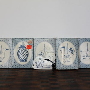 May include: Five blue and white ceramic ornaments in boxes, featuring a duck, pineapple, cat, rooster, and dog. The boxes have a blue and white pattern with small blue birds.