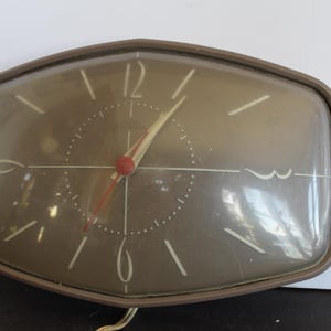 May include: A vintage clock with a brown frame and a gray face. The clock has white numerals and hands, with a red second hand. The clock's face is marked with small white dots. The clock is a retro design.