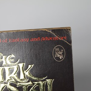 May include: Close-up of a book cover with the title "The Dark Myst" in gold lettering. The text "Tales of Fantasy and Adventure" is printed in red. An owl emblem is visible on the cover.