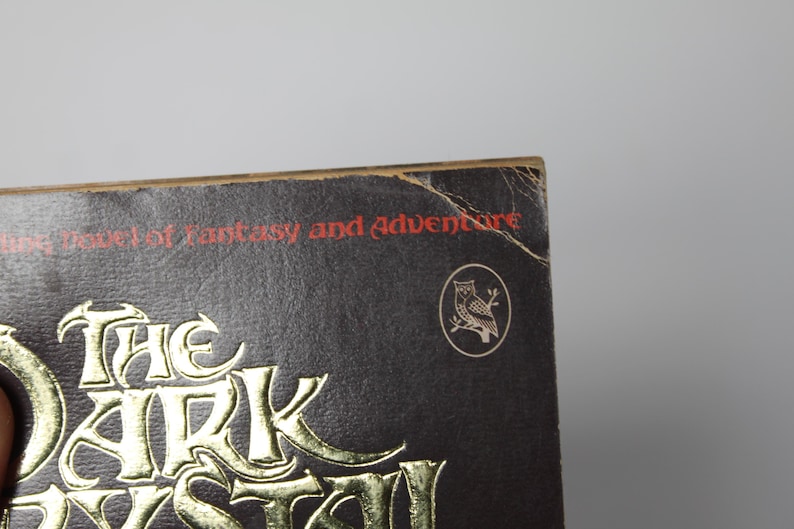 May include: Close-up of a book cover with the title "The Dark Myst" in gold lettering. The text "Tales of Fantasy and Adventure" is printed in red. An owl emblem is visible on the cover.