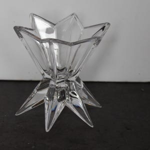May include: Clear glass star-shaped decorative bowl. The bowl has a multi-pointed star design with a wide opening. The bowl is made of clear glass and sits on a black surface.