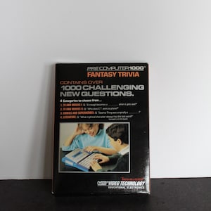 May include: A box for the Pre Computer 1000 Fantasy Trivia game. The box is black with orange text and shows two children playing the game. The text on the box reads "Contains over 1000 Challenging New Questions."