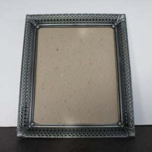 May include: A rectangular, silver-colored picture frame with an ornate, textured border. The frame has a neutral-colored backing and is suitable for displaying photographs or artwork. The frame is made of metal.