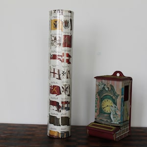 May include: A vintage, red and white matchbox holder with a clock face and a mouse design. The matchbox holder is sitting on a wooden table next to a tube of wrapping paper with a pattern of flags.