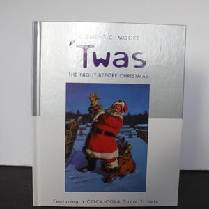 May include: A hardcover book titled "'Twas The Night Before Christmas" by Clement C. Moore. The cover features an illustration of Santa Claus in a red suit, with the text "Featuring a COCA-COLA Santa Tribute".