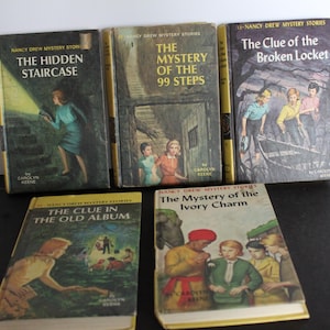 May include: A collection of vintage Nancy Drew mystery books. Titles include "The Hidden Staircase", "The Mystery of the 99 Steps", "The Clue of the Broken Locket", "The Clue in the Old Album", and "The Mystery of the Ivory Charm". The books have yellowed pages and colorful cover illustrations.