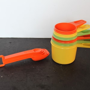 May include: A set of colorful measuring cups and spoons. The cups are stacked in a graduated size, with colors including yellow, orange, green, and red. The spoons are orange and arranged in a row. Kitchen tools.