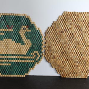 May include: Two hexagonal coasters. One features a swan design in beige and green beads. The other coaster is made of beige beads. The coasters are likely for drinks and are placed on a white surface.