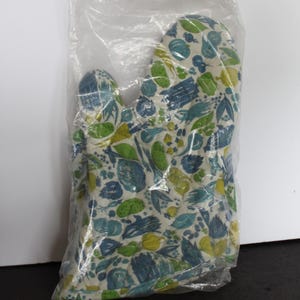 May include: An oven mitt in a clear plastic bag. The mitt features a white background with a pattern of blue, green, and yellow leaves and vegetables. The mitt is designed to protect hands from heat while cooking.