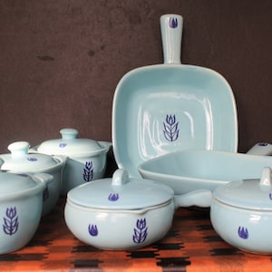 May include: A set of blue and white ceramic cookware with a tulip design. The set includes a large baking dish, a smaller baking dish, and four individual serving dishes with lids.