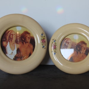 May include: Two cream-colored, round picture frames with floral accents. Each frame holds a vintage photograph of two people. The frames are different sizes, with the larger one on the left.