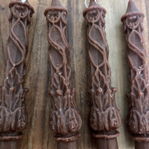 May include: Four brown pillar candles with intricate, ornate designs. Each candle has a pointed top and a thick, decorative base. The candles are arranged vertically, showcasing their detailed carvings and rich color.