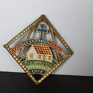 May include: A diamond-shaped wall plaque with a gold-colored frame. The plaque features a house with a red roof, a blue cross, and the words "GOD BLESS THIS HOUSE AND ALL WHO GO IN AND OUT" in various colors.