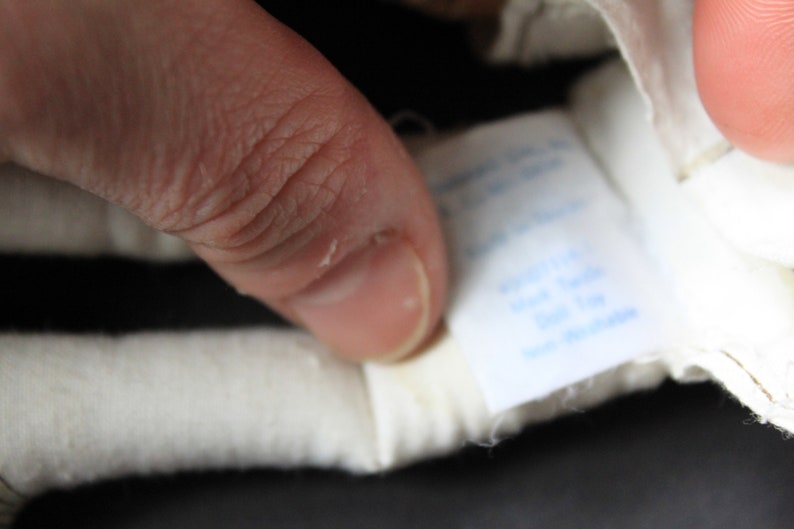 May include: Close-up of a white label with blue text that reads "Exclusive Made in Italy for the USA". The label is attached to a white and black striped fabric.