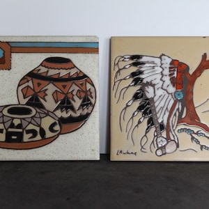 May include: Two square ceramic tiles with Southwestern designs. One tile features pottery in earth tones with geometric patterns. The other tile depicts a Native American headdress and a tree in shades of red, white, and black.