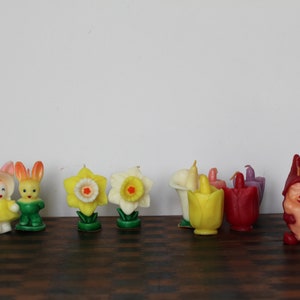 May include: A collection of vintage wax candles featuring a variety of spring themes, including bunnies, flowers, and gnomes. The candles are in various colors, including pink, yellow, green, red, and purple.