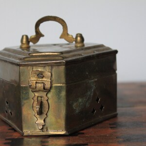 May include: A hexagonal brass box with a hinged lid and a decorative handle. The box has small holes throughout and a brass latch.