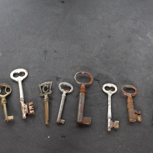 May include: A collection of eight antique keys of varying sizes and designs. The keys are made of metal, with some showing signs of rust and age. The key shapes include oval, heart, and decorative patterns, suggesting a vintage or historical theme.
