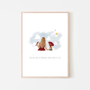 May include: A framed art print featuring a watercolor illustration of a person with long blonde hair in a red dress holding a doll with a red hat. Above them are blue clouds and yellow stars. The text reads, LOVE HAS WAYS OF BRINGING THINGS BACK TO LIFE.