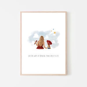 May include: A framed art print featuring a watercolor illustration of a person with long blonde hair in a red dress holding a doll with a red hat. Above them are blue clouds and yellow stars. The text reads, LOVE HAS WAYS OF BRINGING THINGS BACK TO LIFE.