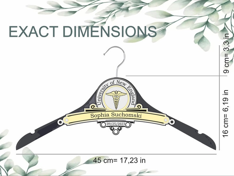 May include: A black clothes hanger featuring a central emblem with the text University of New England and a caduceus symbol. A yellow nameplate reads Sophia Suchomski with the date 09/25/2023. Dimensions are 17.23 inches wide, 6.19 inches high.