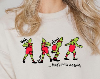 Könnte beinhalten: Ein cremefarbener Pullover mit einer grünen Comicfigur in roten Shorts und einer grünen Mütze. Die Figur ist in vier verschiedenen Posen dargestellt mit dem Text "ooh", "aah", "whhoo" und "...that's it I'm not going".