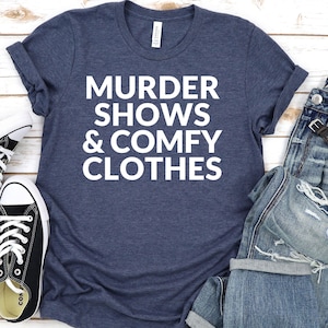 A blue t-shirt with white text, a pair of jeans, and a pair of black and white sneakers are laid out on a wooden surface.