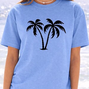 A woman wearing a light blue t-shirt with a graphic of two palm trees printed on it.