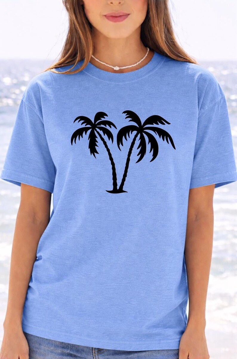 A woman wearing a light blue t-shirt with a graphic of two palm trees printed on it.