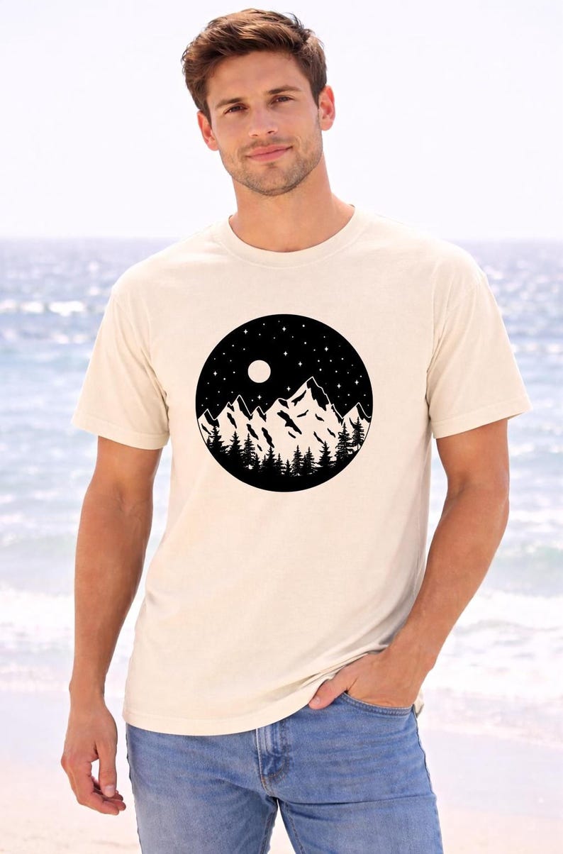 A man wearing a white t-shirt with a graphic design of mountains and a night sky.