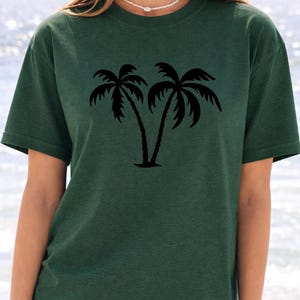 A woman wearing a green t-shirt with a graphic of two palm trees printed on it.