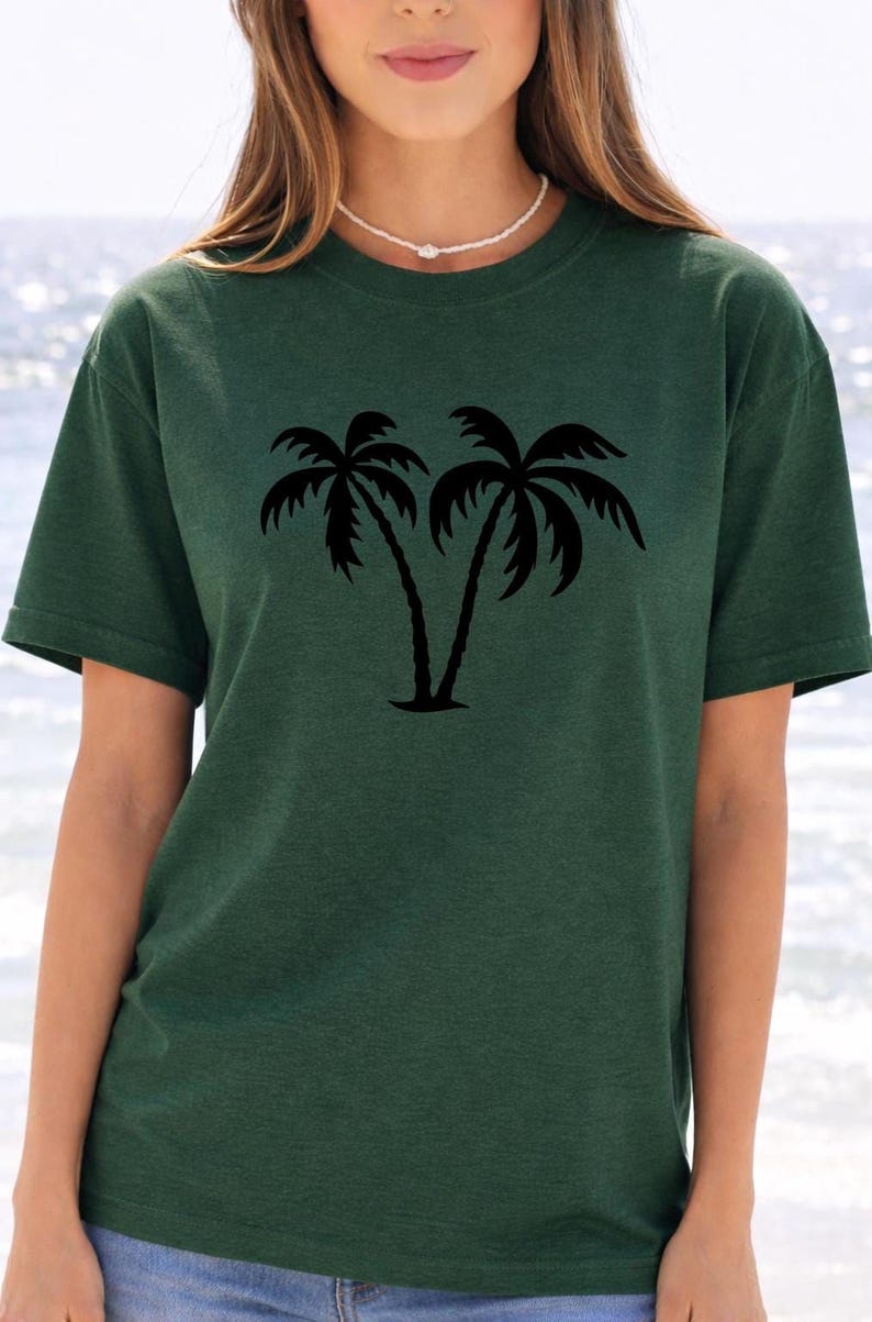 A woman wearing a green t-shirt with a graphic of two palm trees printed on it.