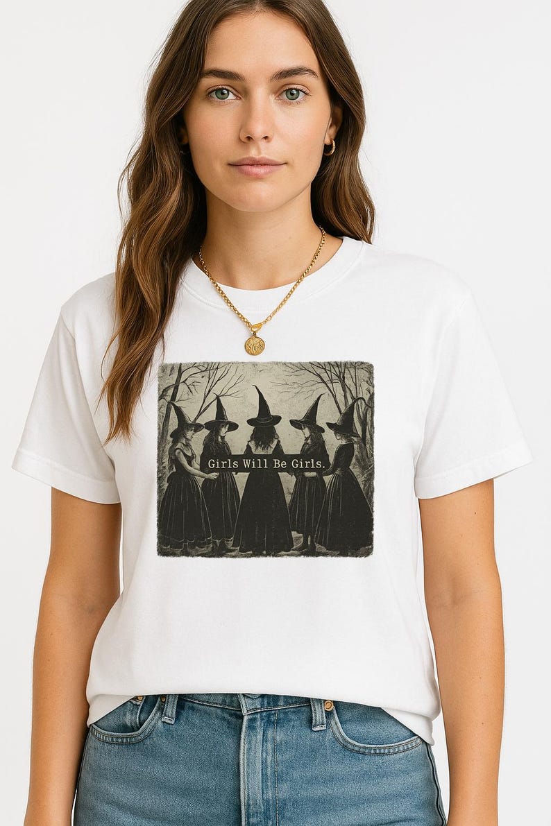 May include: White t-shirt featuring a vintage-style illustration of five figures in witch hats and dresses. The text "Girls Will Be Girls" is printed below the image. The shirt is made of a soft material and has short sleeves.