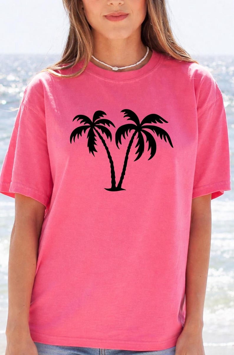 A woman wearing a pink t-shirt with a graphic of two palm trees printed on it.