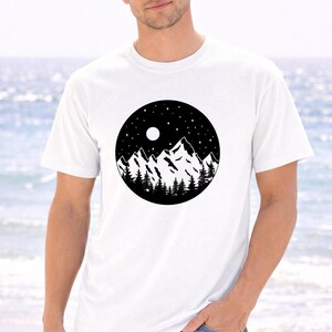 A man wearing a white t-shirt with a black and white graphic of mountains and a night sky.