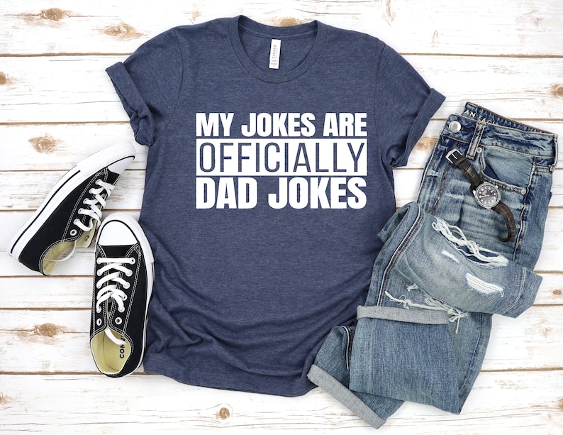 K&ouml;nnte beinhalten: Ein marineblaues T-Shirt mit dem Text "My Jokes Are Officially Dad Jokes" in Wei&szlig;.