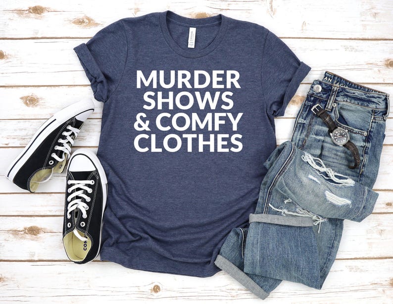 A blue t-shirt with white text, a pair of jeans, and a pair of black and white sneakers are laid out on a wooden surface.