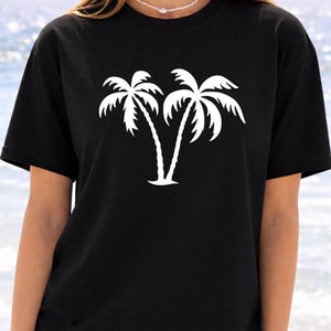 A woman wearing a black t-shirt with a white graphic of two palm trees printed on it.