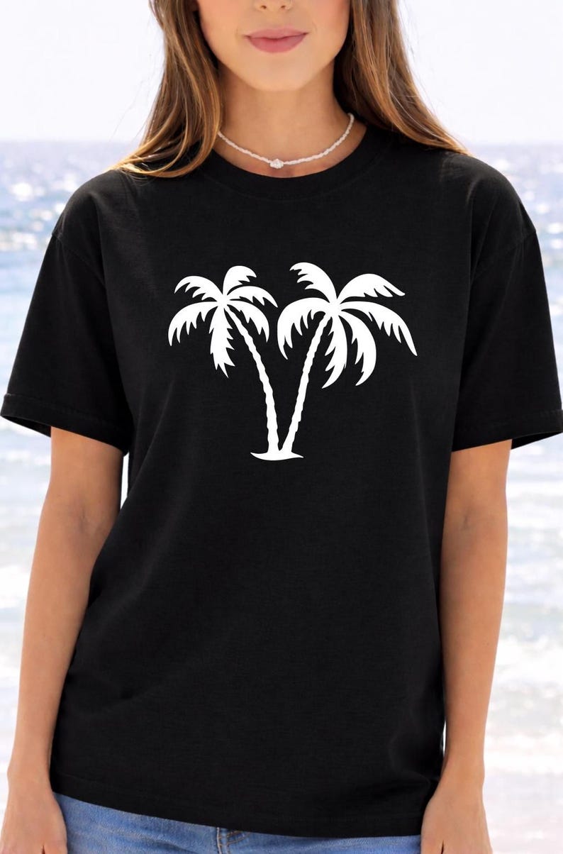 A woman wearing a black t-shirt with a white graphic of two palm trees printed on it.
