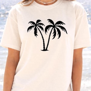 A woman wearing a white t-shirt with a graphic of two palm trees printed on it.