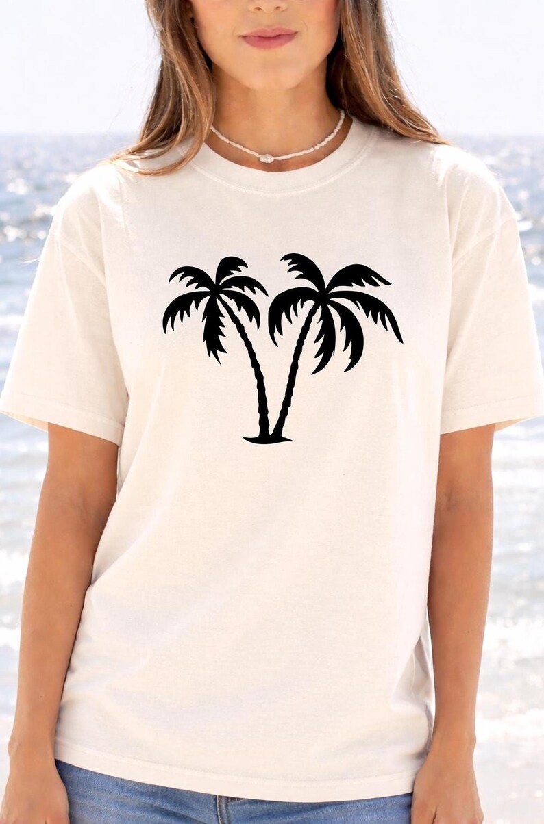 A woman wearing a white t-shirt with a graphic of two palm trees printed on it.