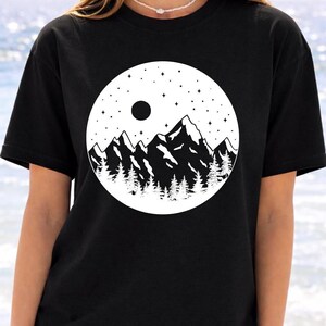 A woman wearing a black t-shirt with a graphic design of mountains and a starry night sky.