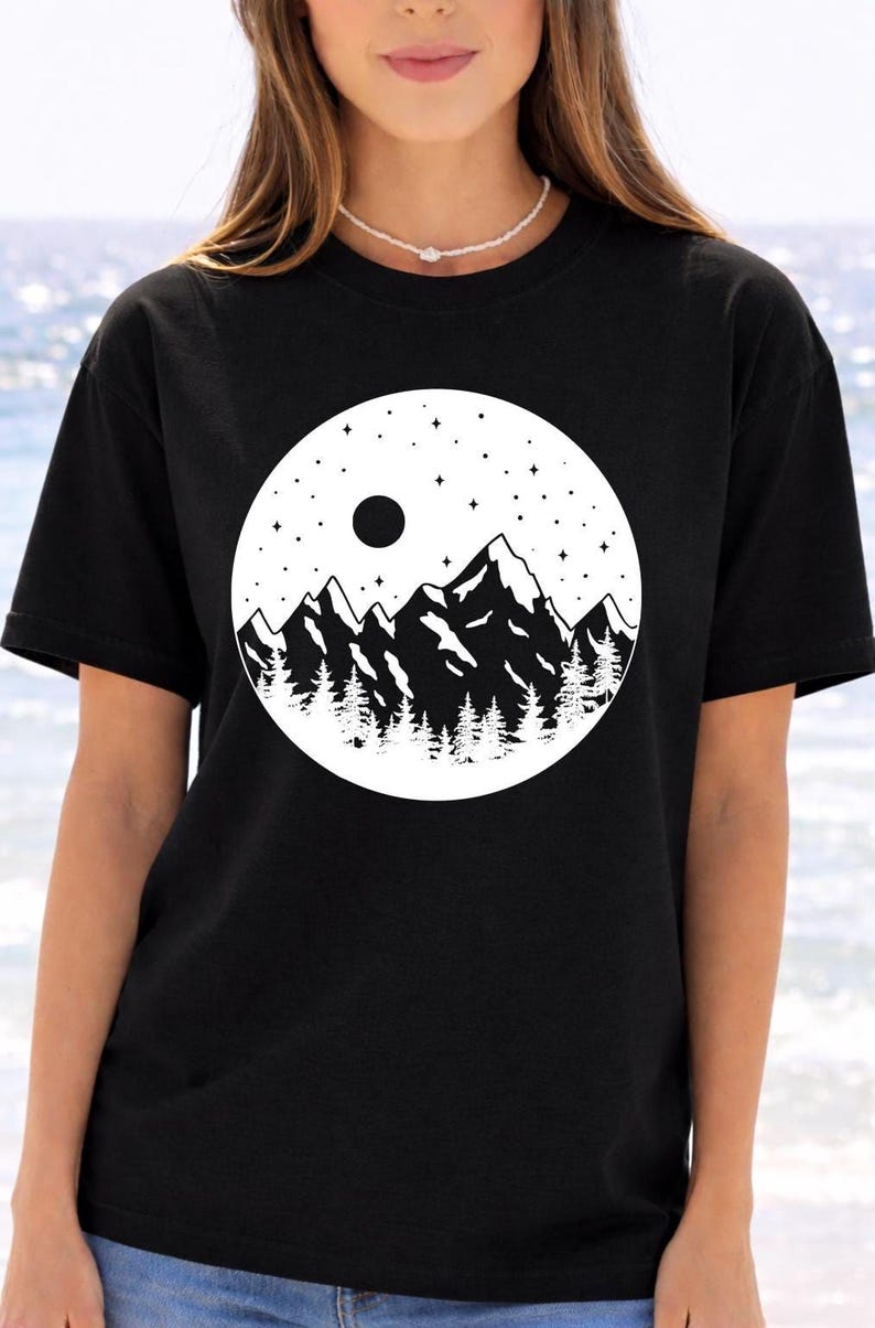 A woman wearing a black t-shirt with a graphic design of mountains and a starry night sky.