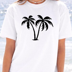 A woman wearing a white t-shirt with a graphic of two palm trees printed on it.