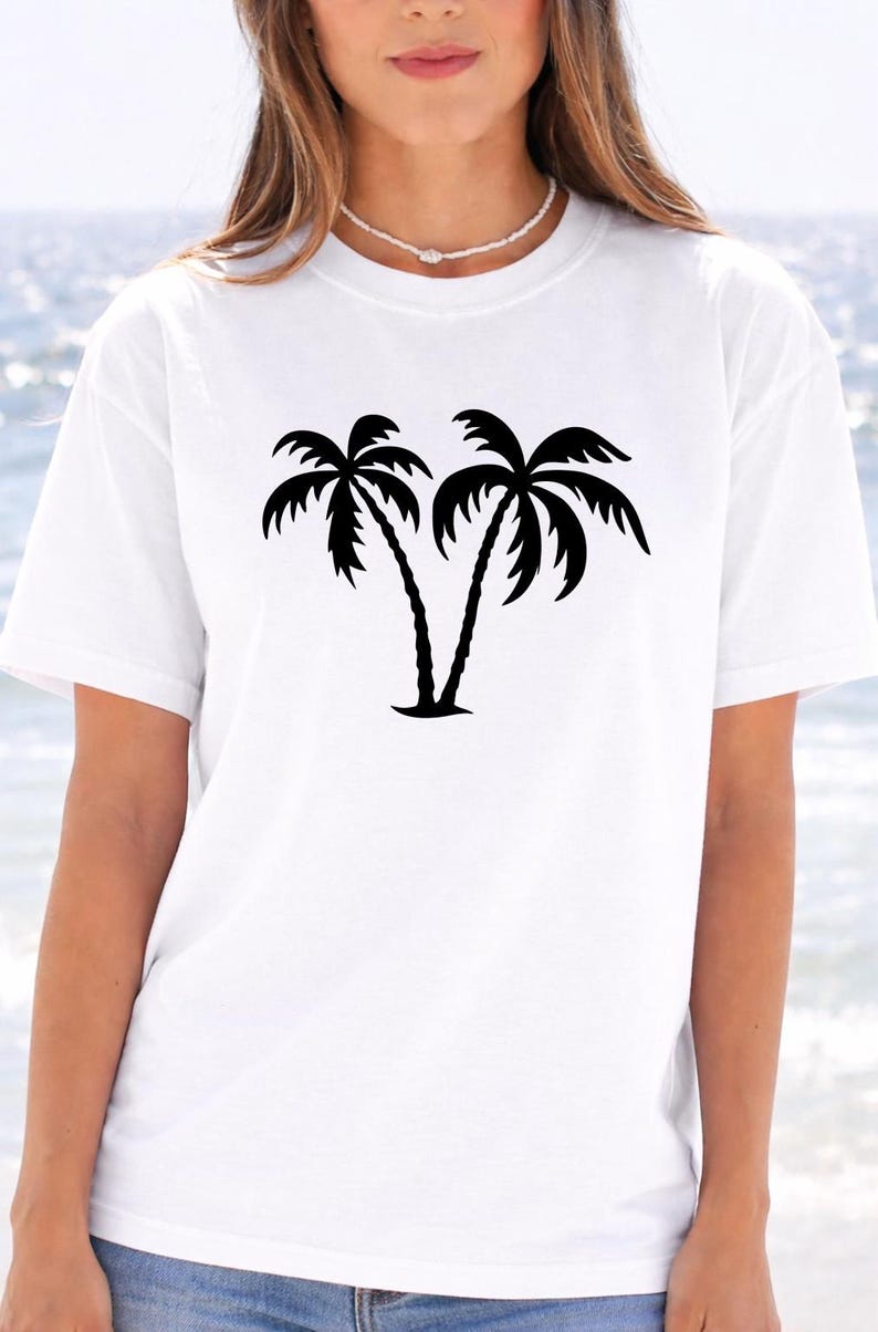 A woman wearing a white t-shirt with a graphic of two palm trees printed on it.