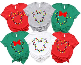May include: A collection of six short-sleeved t-shirts in various colors: red, gray, green, and white. Each shirt features a Mickey Mouse head outline made of colorful Christmas lights. Two green shirts have a red bow.