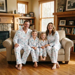 K&ouml;nnte beinhalten: Eine vierk&ouml;pfige Familie tr&auml;gt passende wei&szlig;e Pyjamas mit einem hellblauen und rosa Muster. Die Pyjamas haben ein Hemd mit Kn&ouml;pfen und eine Hose. Die Familie sitzt auf einem beigen Sofa in einem Wohnzimmer mit Kamin und B&uuml;cherregalen.