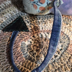 May include: A handcrafted plush toy tail made from blue denim fabric with visible green stitching along the edges. The tail features a triangular black felt tip at the end and is attached to a soft body covered in light blue fabric with an orange fruit pattern.
