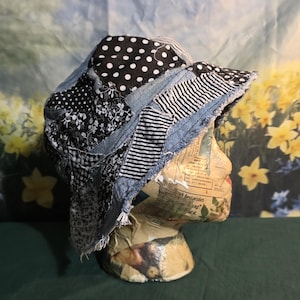 May include: A patchwork bucket hat with a variety of fabrics, including denim, polka dots, floral, and striped patterns. The hat has a frayed brim and is displayed on a mannequin head.
